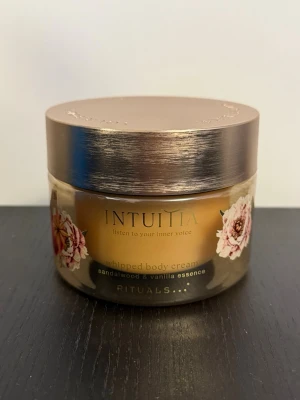 Rituals Intuitia whipped body cream - Lyxig whipped body cream från Rituals i serien Intuitia med doft av sandelträ och vanilj. Burken är guldbrun med blommigt mönster och har ett elegant lock i metallic. Perfekt för dig som vill ha återfuktad och väldoftande hud.