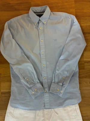 Ljusblå klassisk skjorta - Säljer en stilren ljusblå skjorta med button-down krage och vita knappar. Skjortan har lång ärm och är tillverkad i ett mjukt bomullstyg. Perfekt till både jeans och chinos för en clean look.