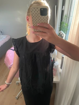 Svart blus/topp med volangärm - Snygg svart blus från Only (nk påsen hänger bara där bak och har inget med bilden och göra) med detaljer och volang vid ärmslut. Blusen har rund halsringning och är gjord i ett lätt bomullstyg. Perfekt för dig som gillar en feminin och stilren look. Den är knappt använd