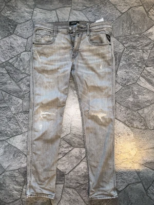 Grå replay jeans med slitningar  - Säljer ett par ljusgrå jeans från Replay med slim fit och slitna detaljer på benen. W 30/31 och 30 i längd. Jeansen har klassisk femficksmodell, dragkedjegylf och är tillverkade i stretchigt denimtyg för extra komfort. Perfekta för en avslappnad och trendig look. Köpt nyligen. Pris kan diskuteras:)