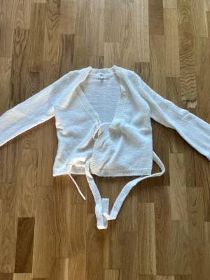 Vit omlottstickad tröja - Säljer en vit stickad omlottopp med långa ärmar och knytband i midjan. 💕 Använd men har inga defekter 