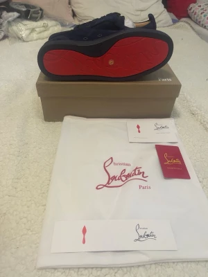 Mörkblå sneakers från Christian Louboutin - Snygga mörkblå sneakers från Christian Louboutin med klassisk röd sula. Skorna har en låg silhuett, rund tå och är tillverkade i mocka med matchande mörkblå skosnören. Insidan är ljusbeige och sulan har den ikoniska loggan. Perfekt för dig som vill sticka ut.