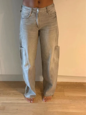 Gråa cargo jeans  - Säljer ett par beige cargo jeans med raka ben och stora sidofickor. Byxorna har normal passform och är tillverkade i bomull. 