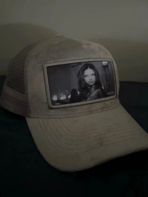 Grå truckerkeps med fototryck - Säljer en grå truckerkeps med mesh på sidorna och ett stort svartvitt fototryck på Adriana Lima framtill. Kepsen har böjd skärm och justerbar baksida. Perfekt för dig som vill sticka ut med en unik accessoar.