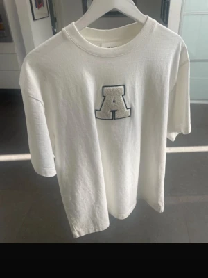 Axel Arigato T shirt  - Vit Axel Arigato t shirt med en stor, broderad bokstav A på bröstet. Klassisk rund hals och avslappnad passform med korta ärmar. Perfekt för dig som gillar enkel men snygg stil.