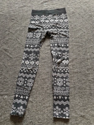 Grå leggings med vintermönster - Mönstrade leggings i grått och vitt med snöflingor, hjärtan och zigzag-detaljer. Mjukt och stretchigt material med bred midjeresår. Perfekta för kalla dagar och riktigt mysiga att ha på sig. 