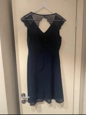 Marinblå spetsklänning från Sisters Point - Snygg marinblå klänning från Sisters Point med spetsdetaljer vid axlar och rygg. Klänningen har v-ringning och är tillverkad i ett lätt, flytande material som ger en elegant siluett. Perfekt för dig som vill ha en stilren look med det lilla extra.