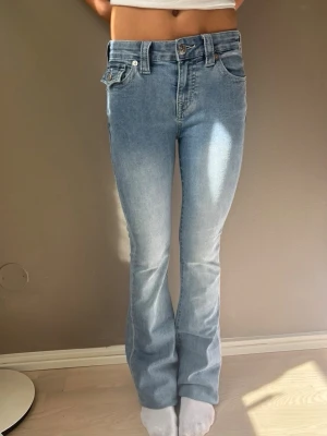 Ljusblå bootcut jeans från true religion  - Säljer ett par ljusblå bootcut jeans med normal midja och klassisk femficksmodell. Jeansen har en snygg tvätt med lätt slitning framtill och utsvängda ben. Perfekta för dig som gillar en retroinspirerad look och vill ha ett par bekväma jeans i mjukt denimtyg. HELT OANVÄNDA