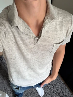 Beige kortärmad piké  - Säljer en beige kortärmad piké i mjukt material. Toppen har en klassisk krage, liten bröstficka och avslappnad passform. Perfekt till jeans eller shorts för en enkel och clean look.