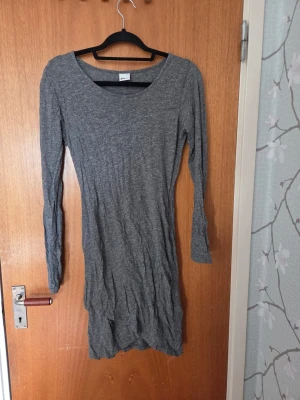Grå långärmad klänning Gina Tricot - En enkel och stilren grå klänning från Gina Tricot. Klänningen har lång ärm, rund halsringning och är gjord i mjukt stretchigt material. Passformen är normal och längden går till strax ovanför knäna. Perfekt basplagg till garderoben.