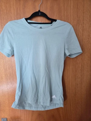 Ljusgrön t-shirt från Adidas - En stilren ljusgrön t-shirt från Adidas med diskret logga nere vid fållen. Klassisk rund hals och korta ärmar. Perfekt till vardags eller träning, tillverkad i mjuk bomull för skön känsla.