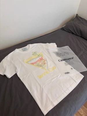 Vit  Tennis Club t-shirt - Säljer en vit t-shirt från Casa med färgglatt tryck och texten 'Tennis Club' på framsidan. T-shirten har rund hals och korta ärmar, perfekt för en avslappnad och sportig stil. Materialet är mjuk bomull som känns skönt mot huden.