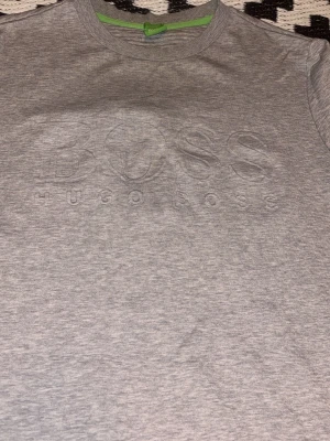 Grå sweatshirt från Hugo Boss - Snygg grå sweatshirt från Hugo Boss med diskret broderad logga på bröstet. Tröjan har rund halsringning, ribbade muddar och är tillverkad i mjukt bomullsmaterial. Perfekt för en avslappnad och stilren look.