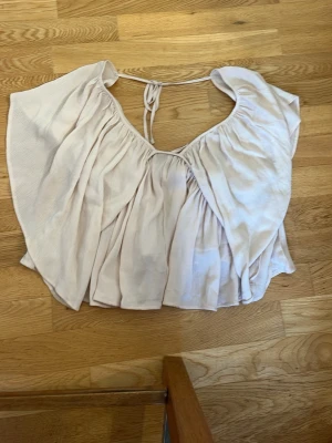 Ljusbeige blus från Gina Tricot - Supersöt ljusbeige blus från Gina Tricot med vida ärmar och knyt i nacken. Blusen har en luftig och flowy passform, perfekt för varma dagar. Tillverkad i ett mjukt tyg som känns skönt mot huden.