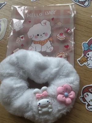 Vit fluffig scrunchie med kanin och blomma - Supersöt vit scrunchie i fluffigt material med dekorationer i form av en liten kanin med rosa rosett och en rosa blomma. Perfekt för att ge en gullig touch till din frisyr och passar dig som gillar kawaii-stil.