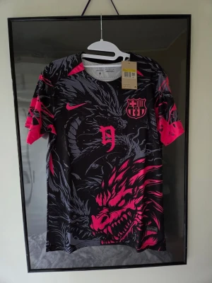 Fotbollströja Fc Barcelona Special Edition  - Riktigt snygg och unik FC Barcelona koncepttröja (Fantasy Kit / Special Edition) med drakmotiv i svart, grått och rosa. Storlek: Small (S) ​Skick: Helt ny och oanvänd med alla lappar kvar.