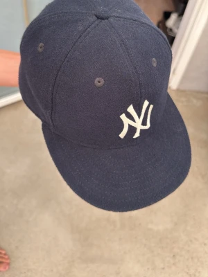 Mörkblå New York Yankees x Fear of God Essentials keps - Snygg mörkblå 59Fifty keps med New York Yankees-logga framtill i vitt och en diskret 'Fear of God'-detalj bak. Klassisk rak skärm och sex paneler med ventilationshål. Tillverkad i ett mjukt tyg som ger en exklusiv känsla. Knappt använd, väldigt, väldigt bra skick. Är lite liten för mig så jag har inte använt den mer än ett par gånger. Inga indikationer på användning förutom lite där framme vid pannan. 