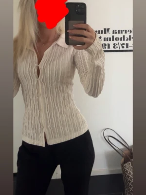 Vit ribbad skjorta med knappar - Säljer en vit långärmad skjorta med ribbad struktur och klassisk krage. Skjortan har knappar framtill och en figurnära passform som ger en snygg siluett. Perfekt att styla med jeans eller kjol för en trendig look.