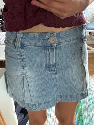 Ljusblå jeanskjol med slitsar - Säljer en snygg ljusblå jeanskjol i klassisk denim med två slitsar framtill. Kjolen har knapp och dragkedja i midjan samt bälteshällor. Perfekt till sommaren eller till hösten med ett par strumpbyxor under och enkel att matcha med olika toppar.