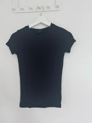 Svart t-shirt - En enkel svart  t-shirt med korta ärmar och rund hals. T-shirten har en tight passform och är perfekt att matcha med jeans eller kjol för en clean look.