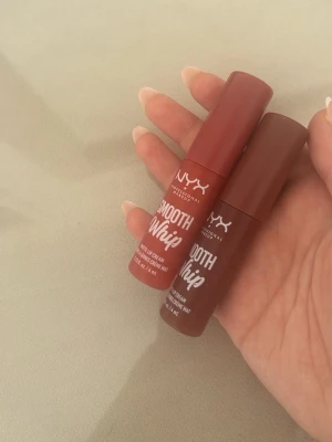 NYX Smooth Whip matt läppglans - NYX Smooth Whip matt läppglans i två olika nyanser av brun och nude. Tuben har en smidig applikator och ger en krämig, matt finish. Perfekt för dig som gillar naturliga färger och vill ha ett mjukt resultat på läpparna.