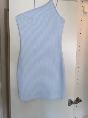 Ljusblå ribbad oneshoulder klänning - Säljer en ljusblå kortklänning med ribbad struktur och oneshoulder-design. Klänningen har tunna axelband och en tight passform som framhäver figuren.