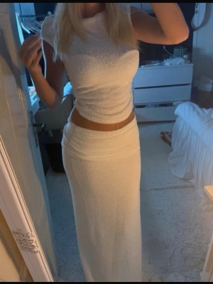Vitt set med lång kjol - Säljer ett stilrent vitt bodyset med en tight, kortärmad topp och en lång, figurnära kjol. Setet har en enkel och clean look med hög midja på kjolen. Materialet ser ut att vara mjukt och stretchigt, perfekt för en trendig och bekväm stil.