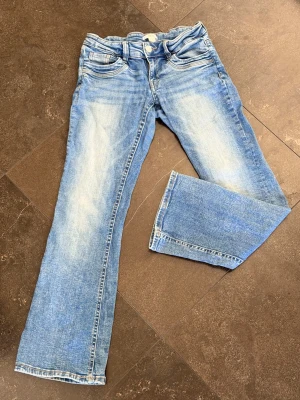 Mörkblå bootcut jeans,ljusa slitningar  - Säljer ett par mörkblå bootcut jeans med slitningar och klassisk femficksmodell. Jeansen har en något utsvängd passform nedtill och är tillverkade i denim med snygg tvätt. Perfekta för en avslappnad och trendig look. Från Gina Tricot 