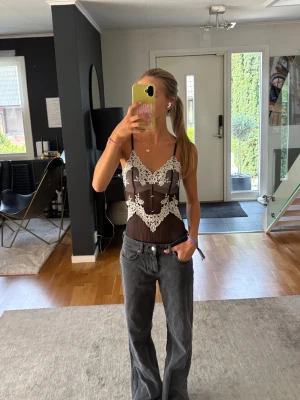 Svart spetsbody med vita detaljer - Supersnygg svart body med tunna axelband och transparent meshmaterial från intimissimi. Bodyn har vita spetsdetaljer och spännbara band. 