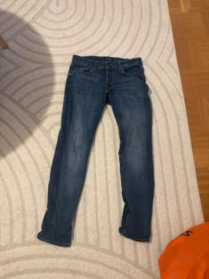 Blå slim fit jeans från Jack & Jones - Snygga blå slim fit jeans från Jack & Jones med klassisk femficksdesign och dragkedjegylf. Jeansen har en lätt tvättad look och kontrastsömmar. Perfekta för en avslappnad och trendig stil.