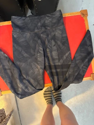 Svarta tights med bladmönster - Snygga svarta tights med diskret bladmönster och hög midja från stonger. Tillverkade i stretchigt funktionsmaterial som passar perfekt för träning eller yoga. Tightsen har en bred linning för extra komfort och sitter tajt längs benen. St S men lappen är borta efter tvättar! Använda men i fint skick!