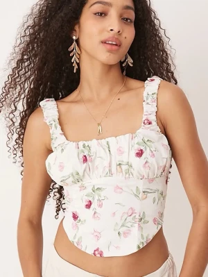 Vit blommig korsettopp med volang - Supersöt vit korsettopp med blommigt mönster i rosa och grönt. Toppen har breda axelband med volangdetaljer och en figurnära passform som framhäver midjan. Perfekt för dig som vill ha en romantisk och trendig look. Oanvänd 