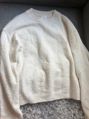 Vit stickad tröja från H&M - Klassisk vit stickad tröja från H&M med rund halsringning och ribbade muddar. Tröjan har en avslappnad passform och är gjord i ett mjukt material som passar perfekt till kyligare dagar. 