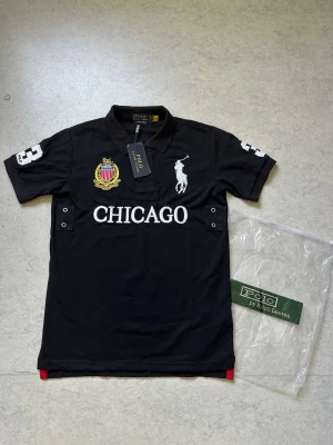 Svart pikétröja Polo Ralph Lauren - Polo Ralph Lauren Chicago  Svart Polo Ralph Lauren Chicago, size S. Stilren och clean modell som är enkel att matcha och passar till det mesta. Fint skick och skön passform.  Skriv gärna om ni är intresserade eller har några frågor!