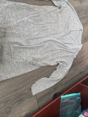 Ljusgrå lång kofta - Mysig ljusgrå lång kofta med öppen front och långa ärmar. Koftan har en mjuk och stretchig känsla, perfekt att slänga på sig över en t-shirt eller topp. Enkel och stilren design som passar till det mesta.