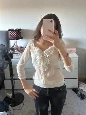Hollister blus med volang och trekvartsärm - Söt vit blus med volangdetaljer längs knäppningen och v-ringning. Blusen har trekvartsärmar och är gjord i ett tunt, lätt material som ger en romantisk känsla. Perfekt att styla med jeans eller kjol för en trendig look.