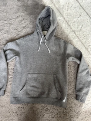 Grå hoodie med Maggiore-tryck - Snygg grå hoodie med stor magficka och huva med vita snören. På ryggen finns ett vitt tryck med texten 'Maggiore' i coolt typsnitt. Tillverkad i mjukt sweatshirtmaterial som känns skönt mot huden. Perfekt för en avslappnad streetwear-look.