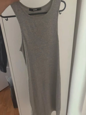 Grå ärmlös ribbad klänning - En enkel och stilren grå klänning i ribbat material. Klänningen är ärmlös och har en rak, kroppsnära passform som passar perfekt till sommaren. Snygg att styla med sneakers eller sandaler.