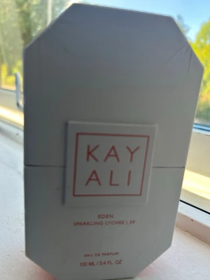 Kayali Eden Sparkling Lychee parfym - Kayali Eden Sparkling Lychee är en Eau de Parfum i en elegant, vit, åttakantig flaska. Doften har noter av svartvinbär, mousserande litchi, ros, sockrad viol, bärnsten och sandelträ. Flaskan rymmer 100 ml och har en modern, stilren design.