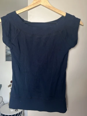 Mörkblå topp från Gina Tricot - En enkel och stilren mörkblå topp från Gina Tricot. Toppen har bred halsringning och är ärmlös med ribbade kanter vid hals och nederkant. Perfekt att matcha med jeans eller kjol för en clean look. Aldrig använd men tagit bort lappen