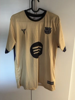 Gul FC Barcelona matchtröja nr 10 - Snygg gul FC Barcelona matchtröja med svarta detaljer och tryck. Tröjan har klubbmärke på bröstet, sponsorlogga framtill och Lamine Yamal samt nummer 10 på ryggen. Tillverkad i lätt och ventilerande material, perfekt för fotboll eller träning.