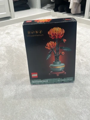 LEGO Botanicals Chrysanthemum - Säljer ett LEGO Botanicals set, Chrysanthemum, med 278 delar. Byggsatsen föreställer en orange och gul blomma i kruka och kommer i en snygg svart förpackning. Perfekt för dig som gillar byggsatser och inredning med en twist.