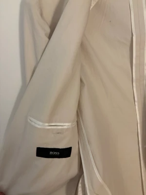 Beige kavaj från BOSS - Stilren beige kavaj från BOSS med två knappar framtill och klassisk krage. Kavajen har diskreta fickor och är helfodrad med ljusa detaljer på insidan. Perfekt för en dressad look och passar till många olika outfits. Riktigt go sommar/höst kavaj. Nypris 2199kr. Matieralt är grymt. 