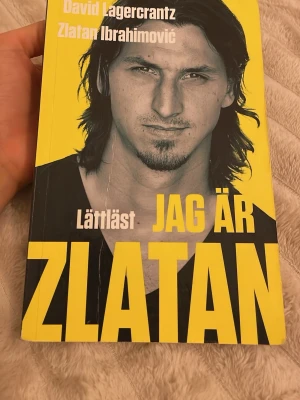 Jag är Zlatan lättläst pocketbok - Pocketbok med gul och svart framsida, titeln 'Jag är Zlatan' i stora bokstäver och ett porträtt av Zlatan Ibrahimović. Boken är skriven av David Lagercrantz och Zlatan Ibrahimović och är en lättläst version utgiven av LL-förlaget.