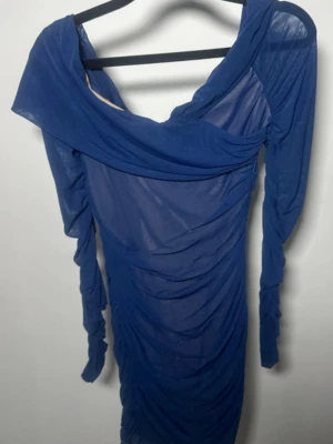 Blå långärmad omlottklänning - Snygg blå klänning med lång ärm och omlott-detalj upptill. Klänningen har rynkade partier längs hela kroppen och är tillverkad i ett tunt, lätt material som ger en cool look. Perfekt för dig som vill sticka ut med en trendig och unik stil.
