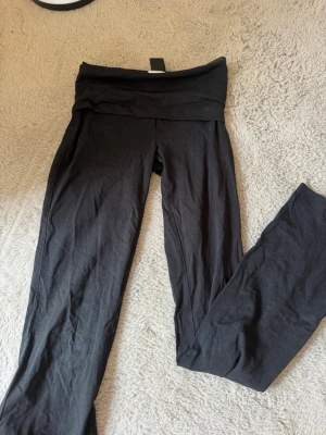 Svarta yoga pants - Säljer ett par svarta yoga pants med bred, vikbar linning i midjan. De är mjuka och stretchiga, perfekta för en avslappnad och bekväm stil. Materialet känns som bomullsmix och passformen är bootcut. 