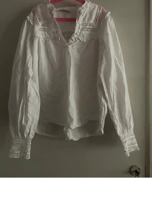Vit blus med spets från Holly & Whyte - Vit blus från Holly & Whyte by Lindex med långärmad design, smockdetaljer vid ärmslut och axlar samt v-ringad hals. Blusen har ett luftigt tyg och dekorativa broderier upptill. Perfekt för en trendig och avslappnad look. Tröjan är använd endast ett fåtal gånger eftersom den är för liten. Storlek S men passar till M med. Diskuterar mer än gärna pris! ❤️