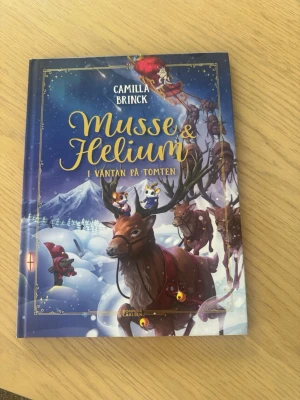 Musse & Helium: I väntan på tomten - En färgglad och vintrig barnbok med hårda pärmar, skriven av Camilla Brinck. Omslaget visar Musse och Helium på en ren i ett snöigt landskap med tomten och nissar. Perfekt för dig som gillar magiska äventyr och julstämning.