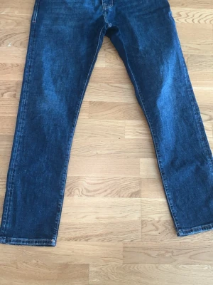 Mörkblå raka jeans - Ett par klassiska mörkblå jeans med rak passform och fem fickor. Jeansen har en enkel design utan synliga loggor och är tillverkade i denim. Perfekta för en avslappnad och stilren look.