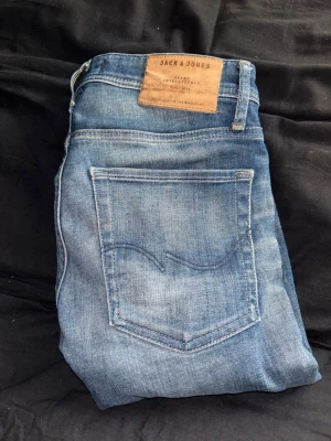 Blå jeans från Jack & Jones - Snygga blå jeans från Jack & Jones med klassisk femficksdesign och slitna detaljer framtill. Jeansen har en rak passform och är gjorda i mjuk denim med en cool tvättad look. Perfekta för en avslappnad och trendig stil.